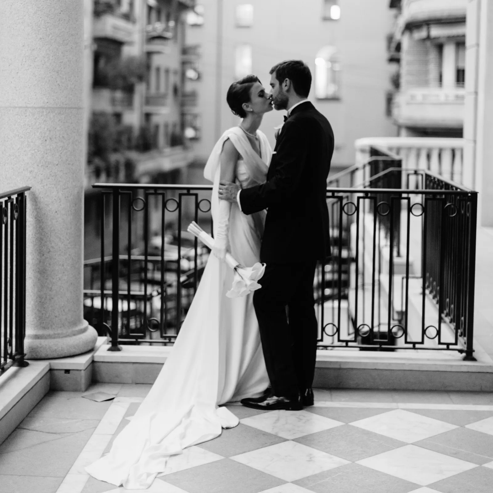 Foto in bianco e nero di una sposa e uno sposo che si baciano su un balcone